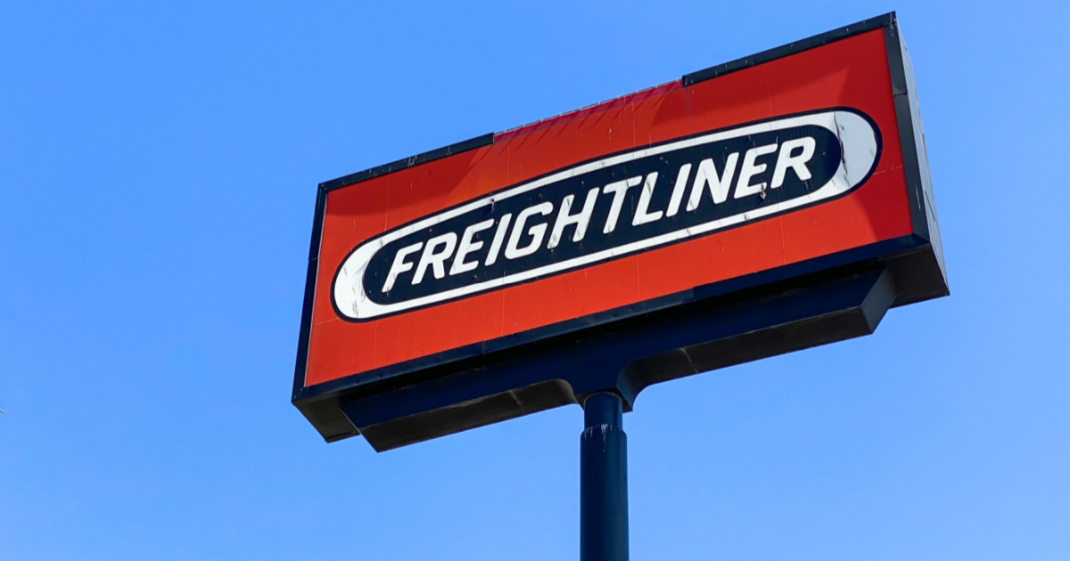 Red Freightliner billboard sign in front of blue sky.