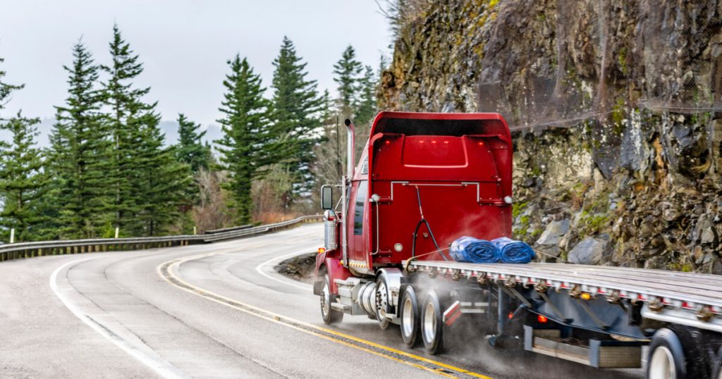 red semi on a highway in the mountains with tress