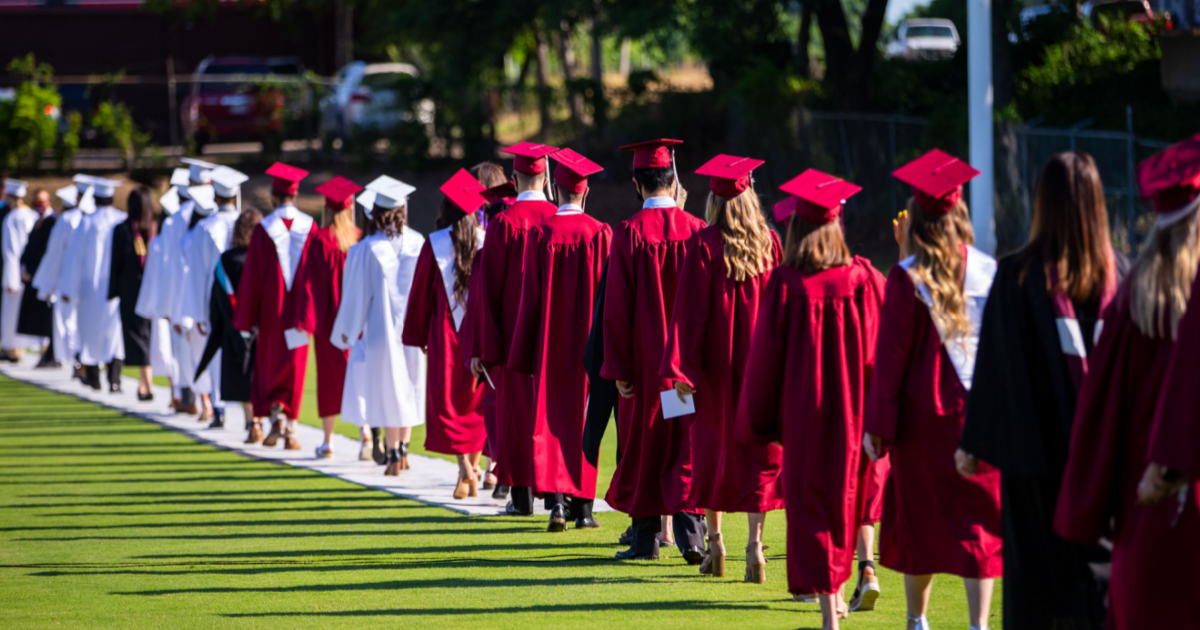 Image of a graduation ceremony. Students are in a line wearing white and red gowns.